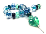 The patterned beads have cores of Tuscan Teal and Trade Winds encased in Effetre Pale Aquamarine and are decorated with Effetre Periwinkle. The heart is CiM Absinthe.